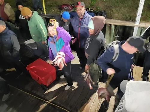People on a dock with fishing gear and caught fish.